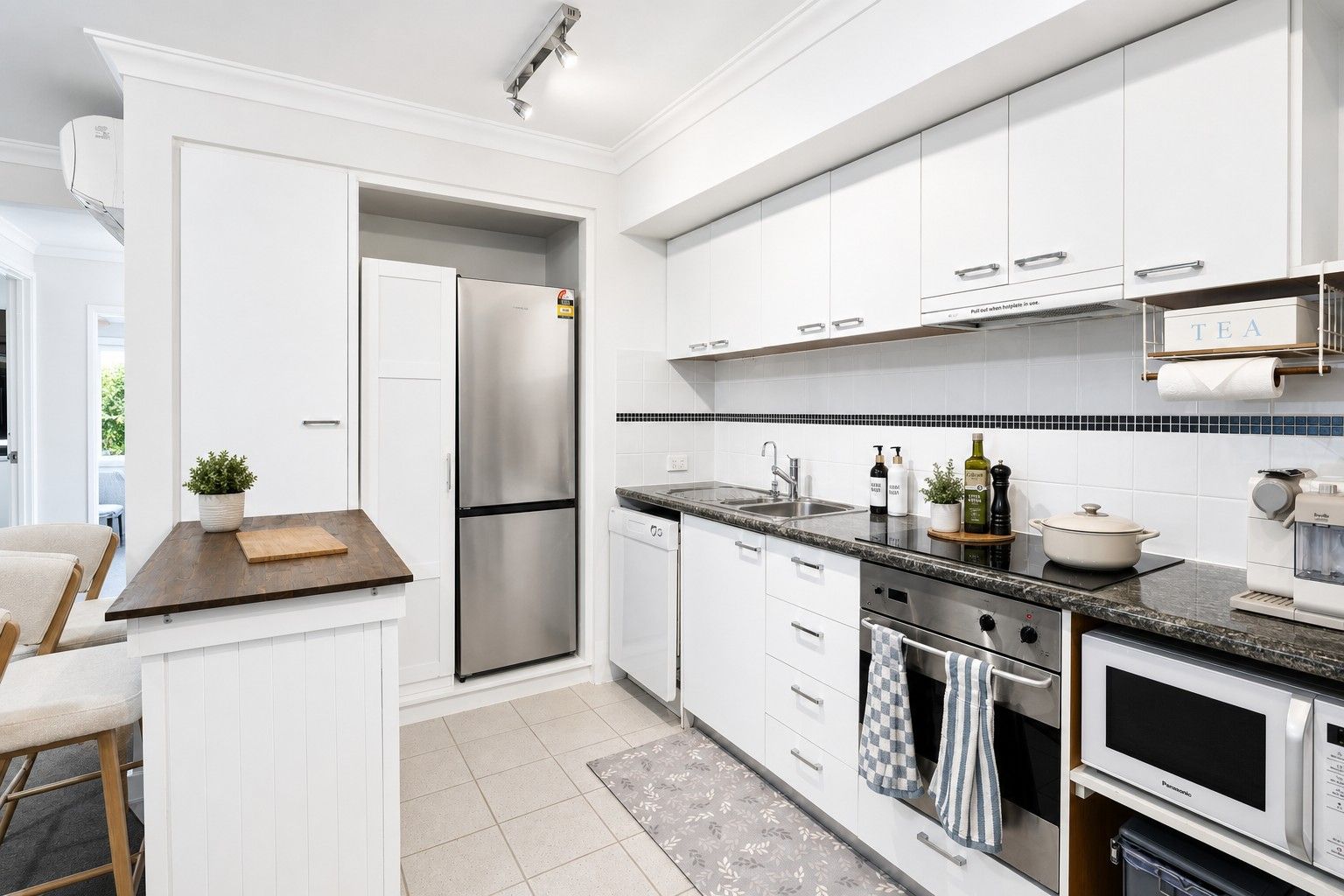 A modern kitchen with white cabinetry, a stainless steel refrigerator, a built-in oven, and a microwave.