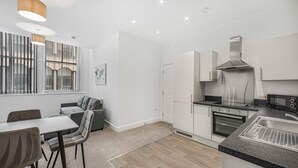 A modern kitchen with white cabinets, a built-in oven, a microwave, and a gas stove. There is a dining area with a table and chairs, and a sofa. - GuestReady - Fantastic Liverpool getaway (Liverpool)