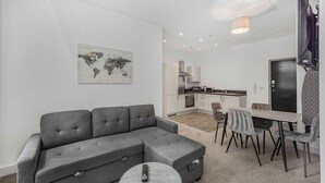 A modern living room with a grey sectional sofa, a round coffee table, and a dining area with a table and chairs. - GuestReady - Fantastic Liverpool getaway (Liverpool)