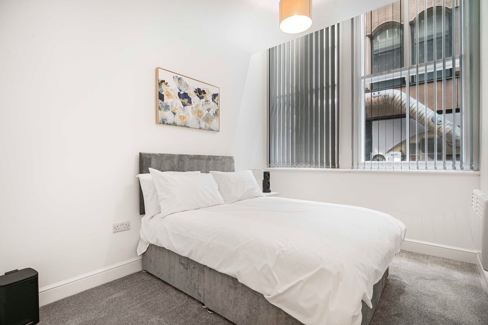 Une chambre à coucher avec un lit, une fenêtre avec des stores, un radiateur et un tableau accroché au mur.
