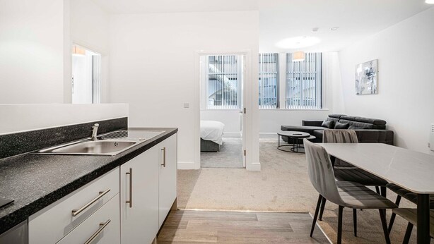 A modern kitchen with a granite countertop and stainless steel sink, a dining area with a table and chairs, and a living room with a sofa and a coffee table. - GuestReady – Modern comfort in Liverpool (Liverpool)