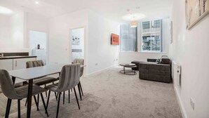 A modern hotel room with a dining area, a sofa, and a large window with blinds. - GuestReady – Modern comfort in Liverpool (Liverpool)