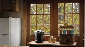 A kitchen with a refrigerator, coffee maker, and jars on the counter, and a window with a view of trees. - The Serenity Cabin | Firepit | Wineries | Hiking (Marshall)