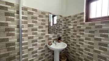 Un baño con pared de azulejos, un lavamanos, un espejo y una ventana.