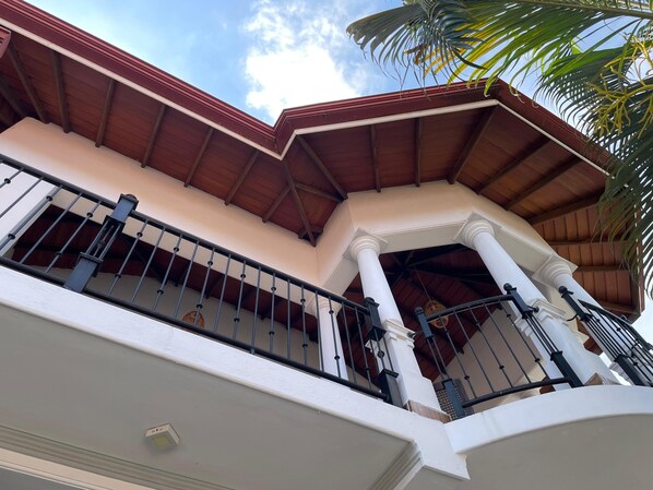 A corner of a building with a red roof, white columns, and a balcony with black railings. - BlissFam Villa & Hostel (Negombo)