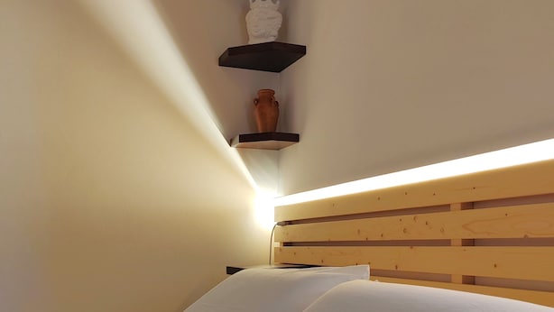 A bedroom with a wooden headboard, a bed with white bedding, and a wall-mounted shelf with a pineapple, a vase, and a small statue. - Domus Amelio - Country Rooms (Cinisi)