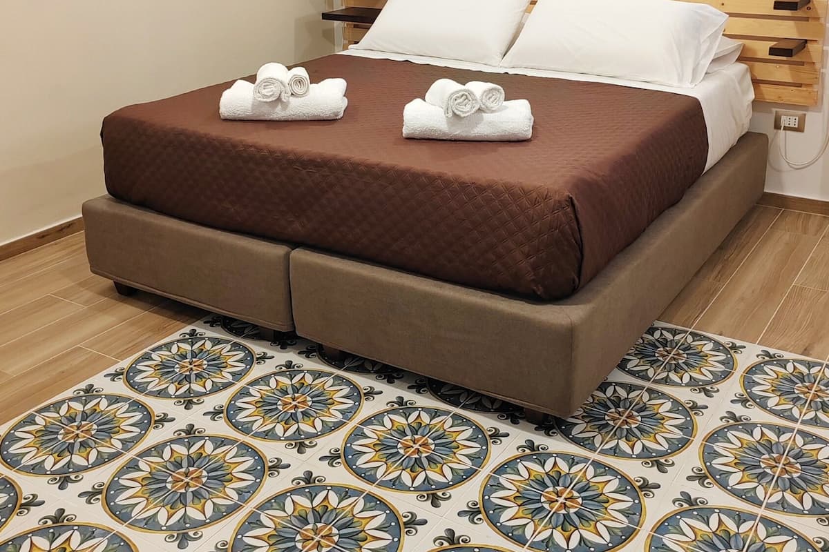 A neatly made bed with a brown bedspread and white pillows, a wooden headboard, and a patterned tile floor.