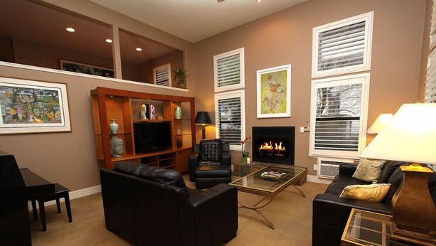 A living room with a fireplace, black leather sofas, a glass coffee table, and a wooden entertainment unit.