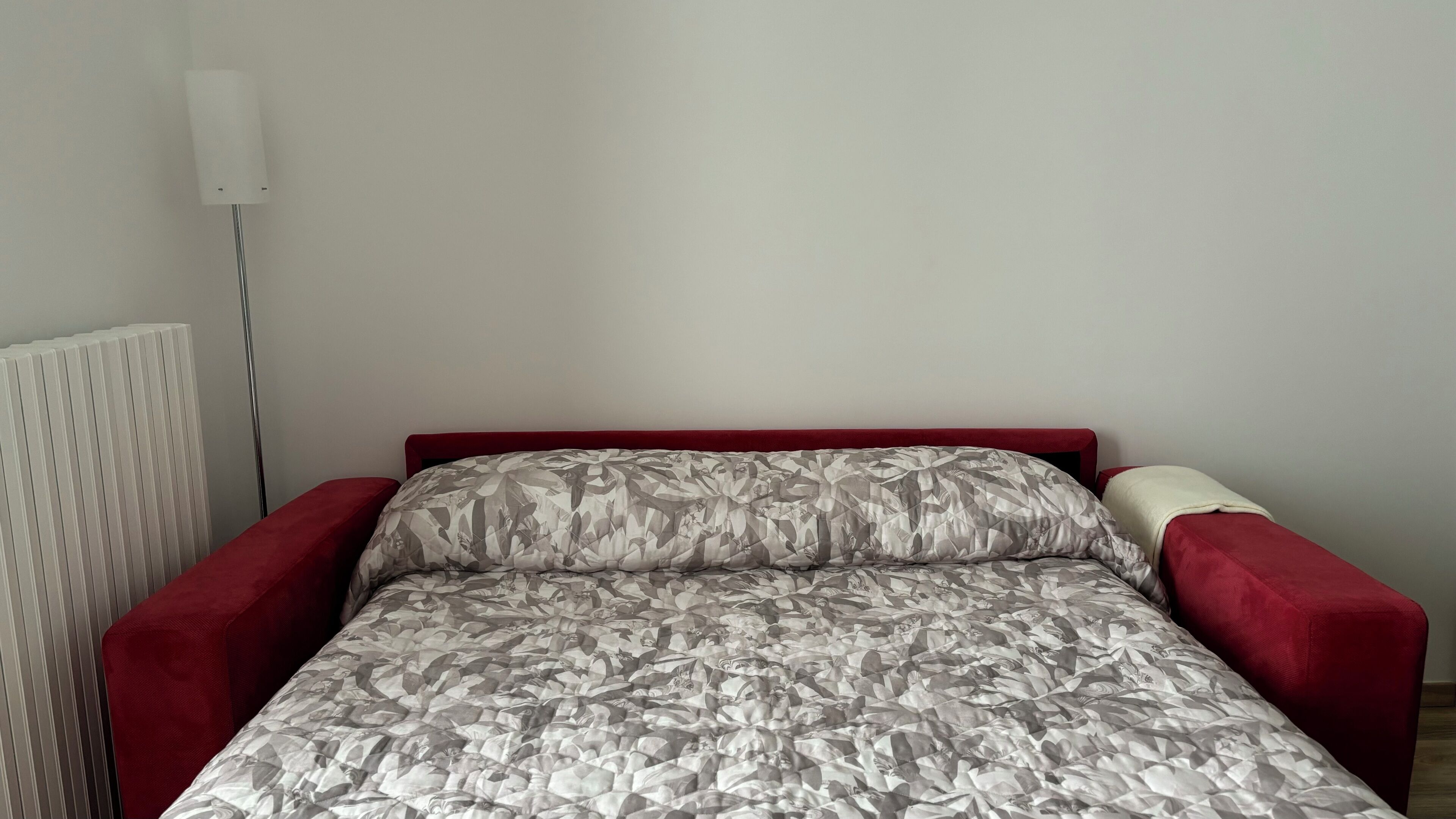 Un lit simple avec une couvre-lit à motifs, une tête de lit rouge et des accoudoirs assortis de la même couleur.