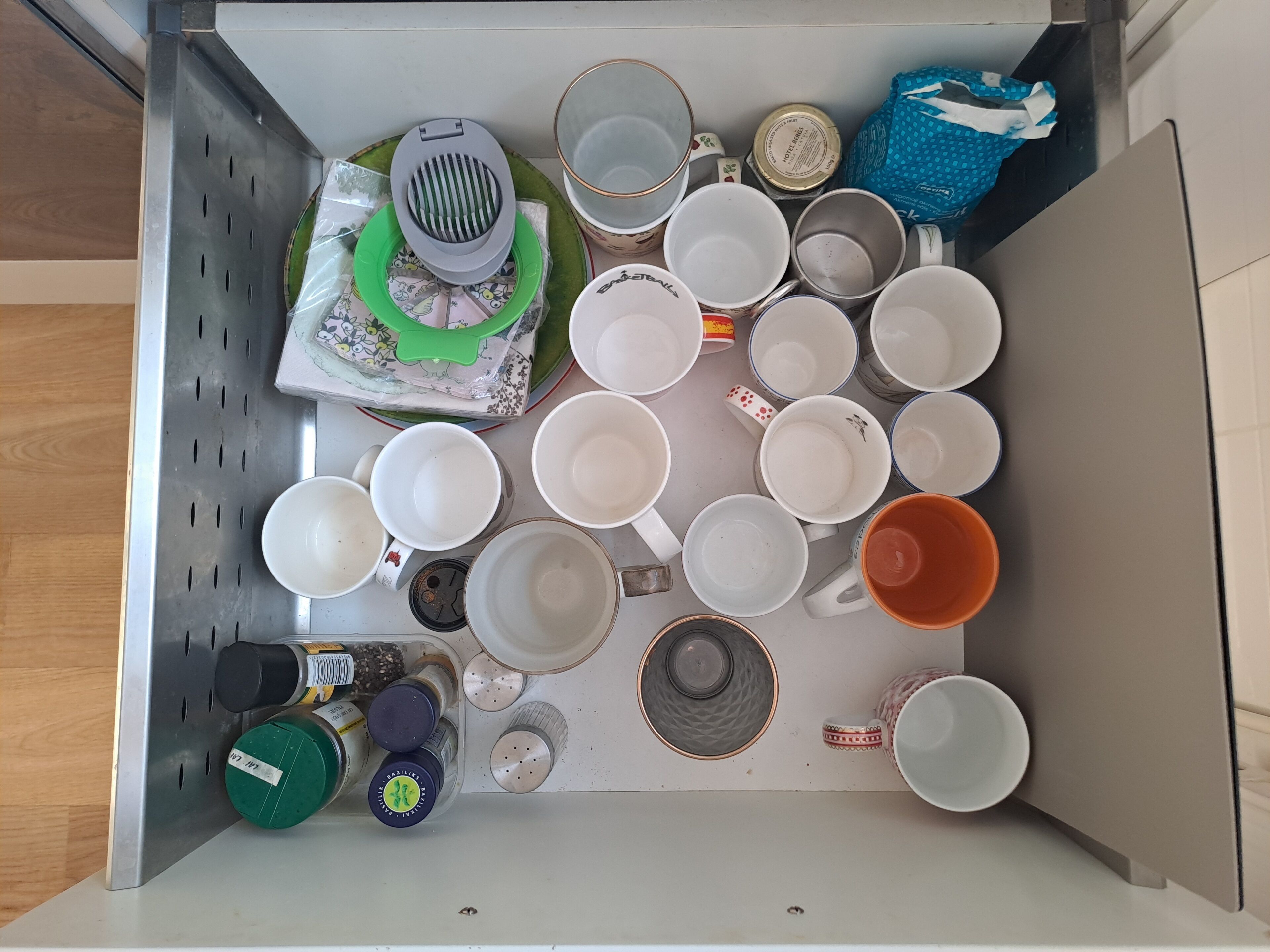 Un cassetto contiene diversi oggetti da cucina, tra cui tazze, un colino e contenitori per spezie.