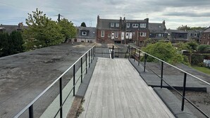 A rooftop with a wooden deck and metal railings, overlooking residential buildings.