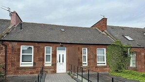 A two-story brick building with a white door and windows, a wooden deck with black railings, and a brick chimney.