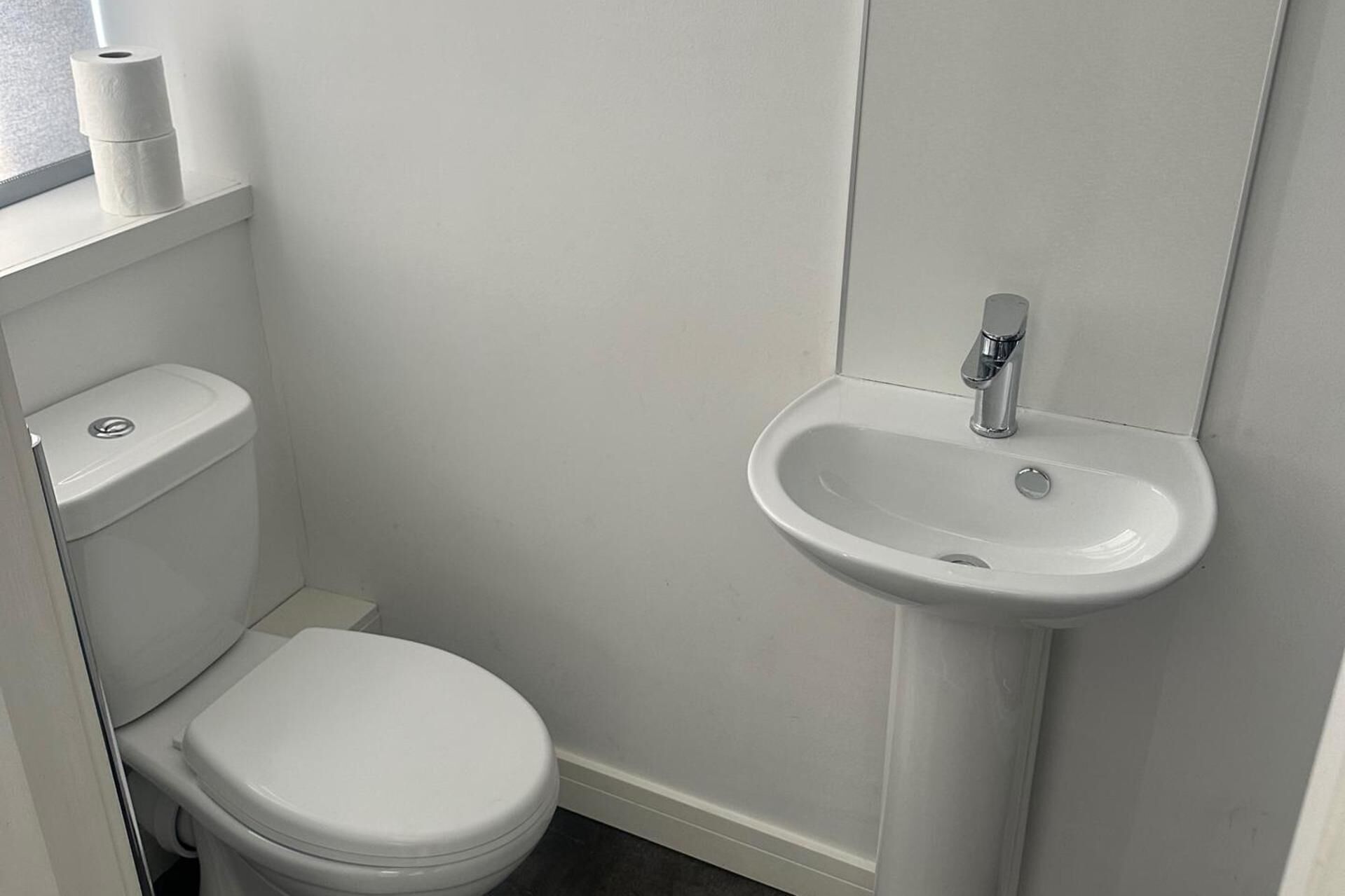 Une petite salle de bain propre, avec des toilettes, un lavabo et un rouleau de papier toilette accroché au mur.