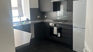 A modern kitchen with dark cabinetry, a built-in oven, a refrigerator, and a window providing natural light.