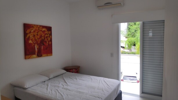 Un dormitorio con cama, un cuadro, aire acondicionado y vista al exterior.