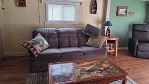 A living room with a grey sofa, a coffee table with a collage, a wooden side table, and a green wall. - Offut Lake!  Pet friendly cottage with lake access..  Bring your fishing rod! (Tenino)