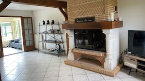 A living room with a brick fireplace, a wooden TV stand, and a shelving unit with decorative items. - Ma belle Normande entre terre & mer - My beautiful Normandy between land and sea (Saint-Léonard)