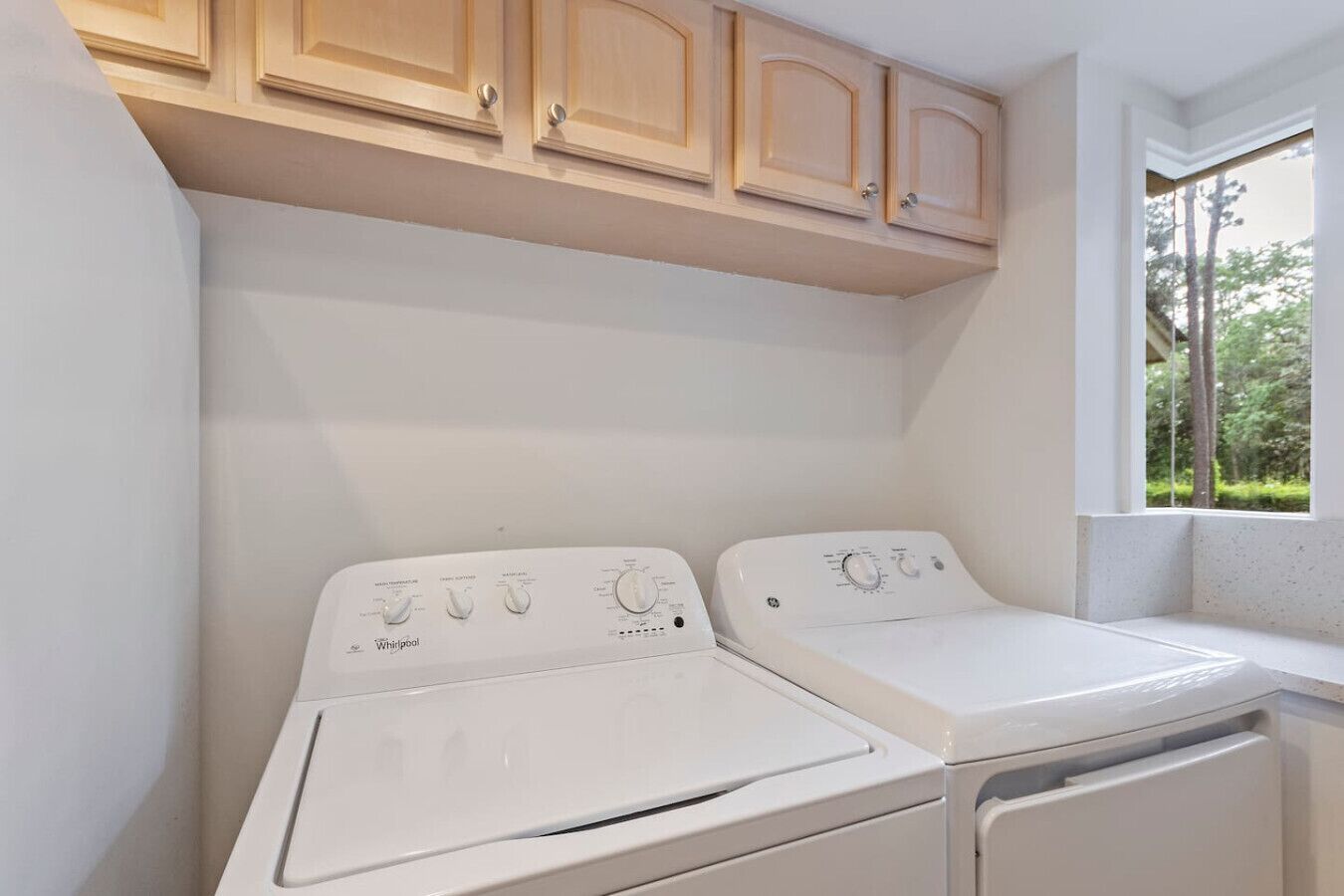 Une buanderie équipée de deux lave-linge Whirlpool et de meubles de rangement en bois au-dessus.