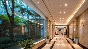 A modern hotel lobby with a glass wall, a marble floor, and potted plants. - Jingyuan Shuizhuang Hotel (Shanghai)