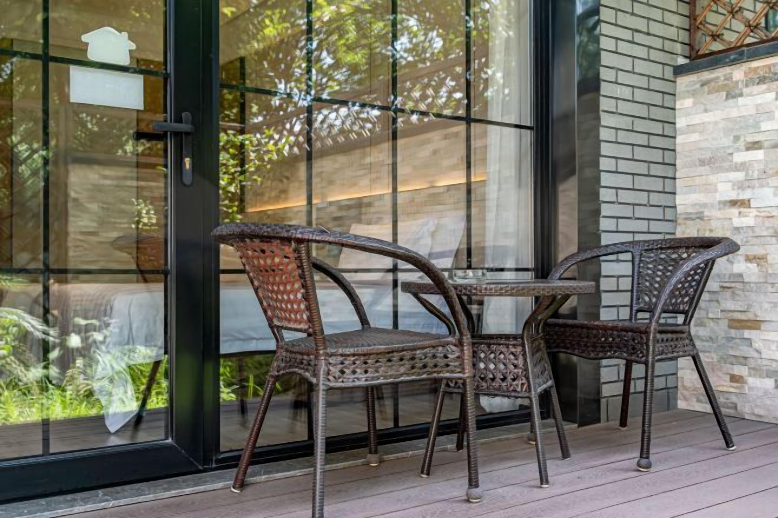 A patio with wicker chairs and a table, a glass door, and a brick wall.