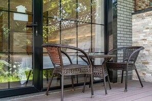 Un patio con sillones de mimbre, una mesa, un vidrio y un muro de ladrillo.