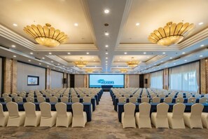 A conference room with rows of chairs, a large screen, and chandeliers.