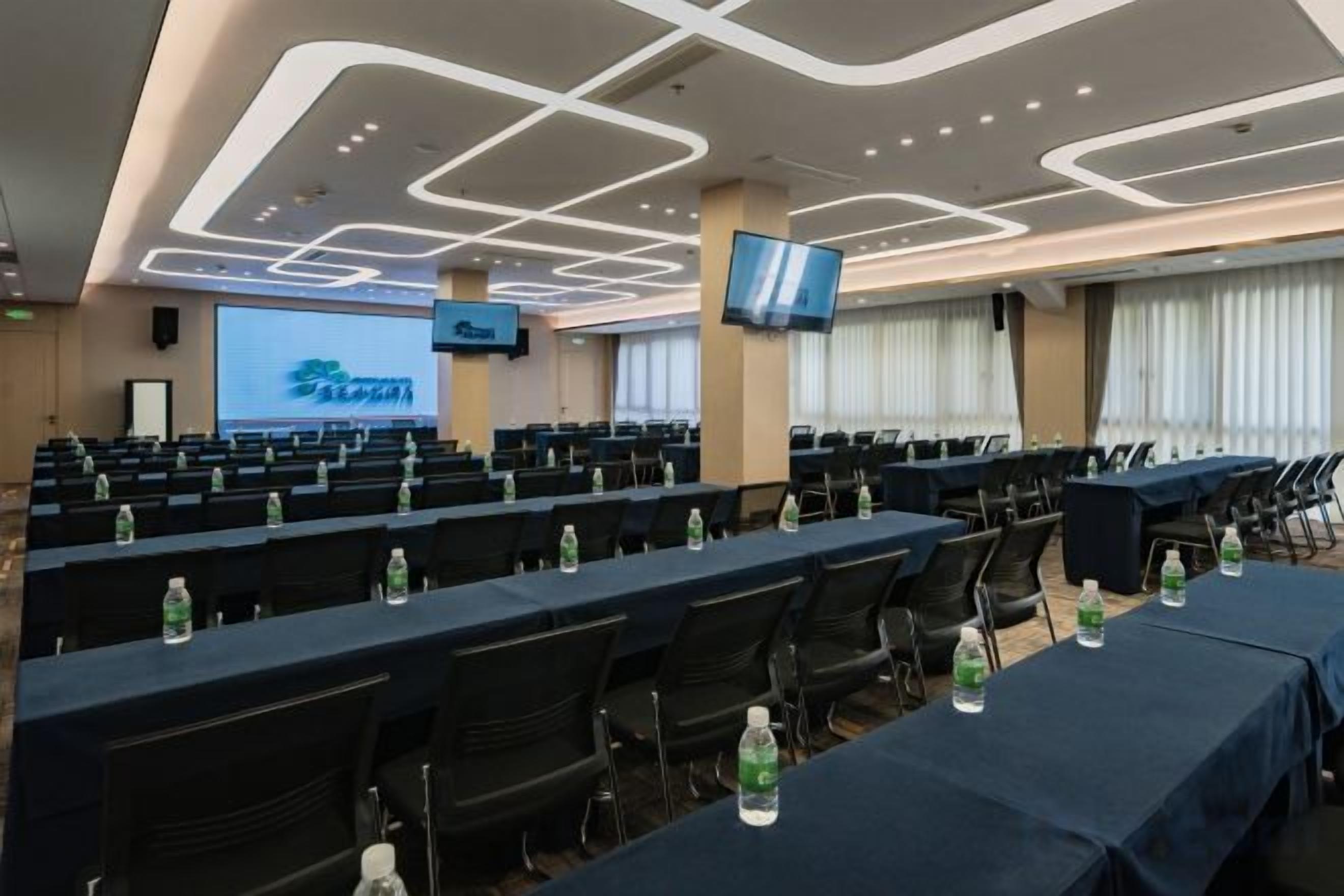 A conference room with rows of tables, chairs, and a large screen.