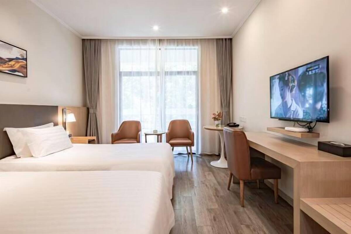 A hotel room with two beds, a desk, a chair, a TV, and a window with curtains.
