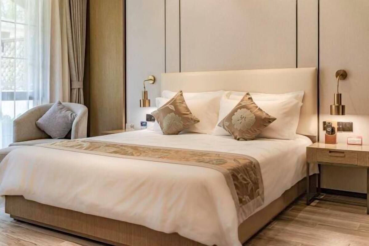 A hotel room with a large bed, a bedside table, a lamp, and a window with curtains.