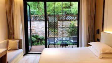 A bedroom with a large bed, a sofa, and a view of a garden through a glass door.