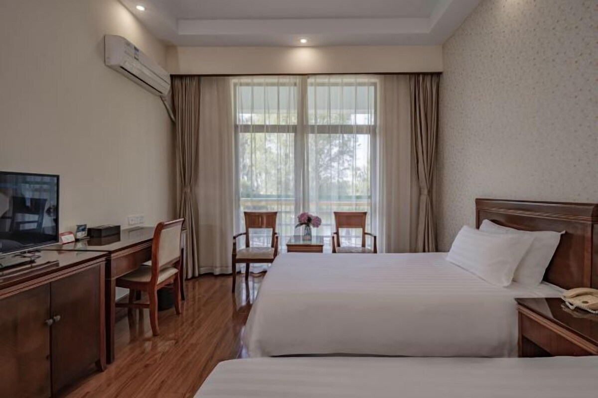 Habitación de hotel con cama, escritorio, silla, televisor y ventana con cortinas.