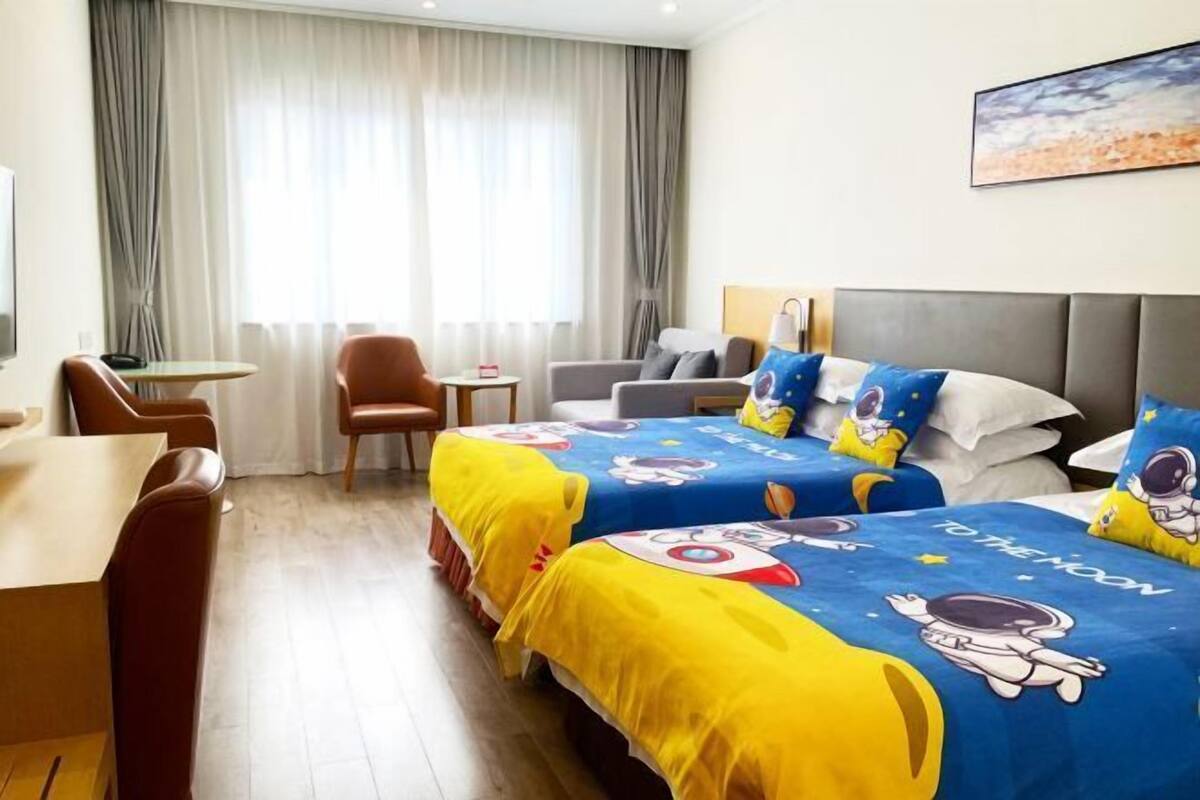 A hotel room with two beds, a desk, a chair, and a view of the outdoors through large windows.