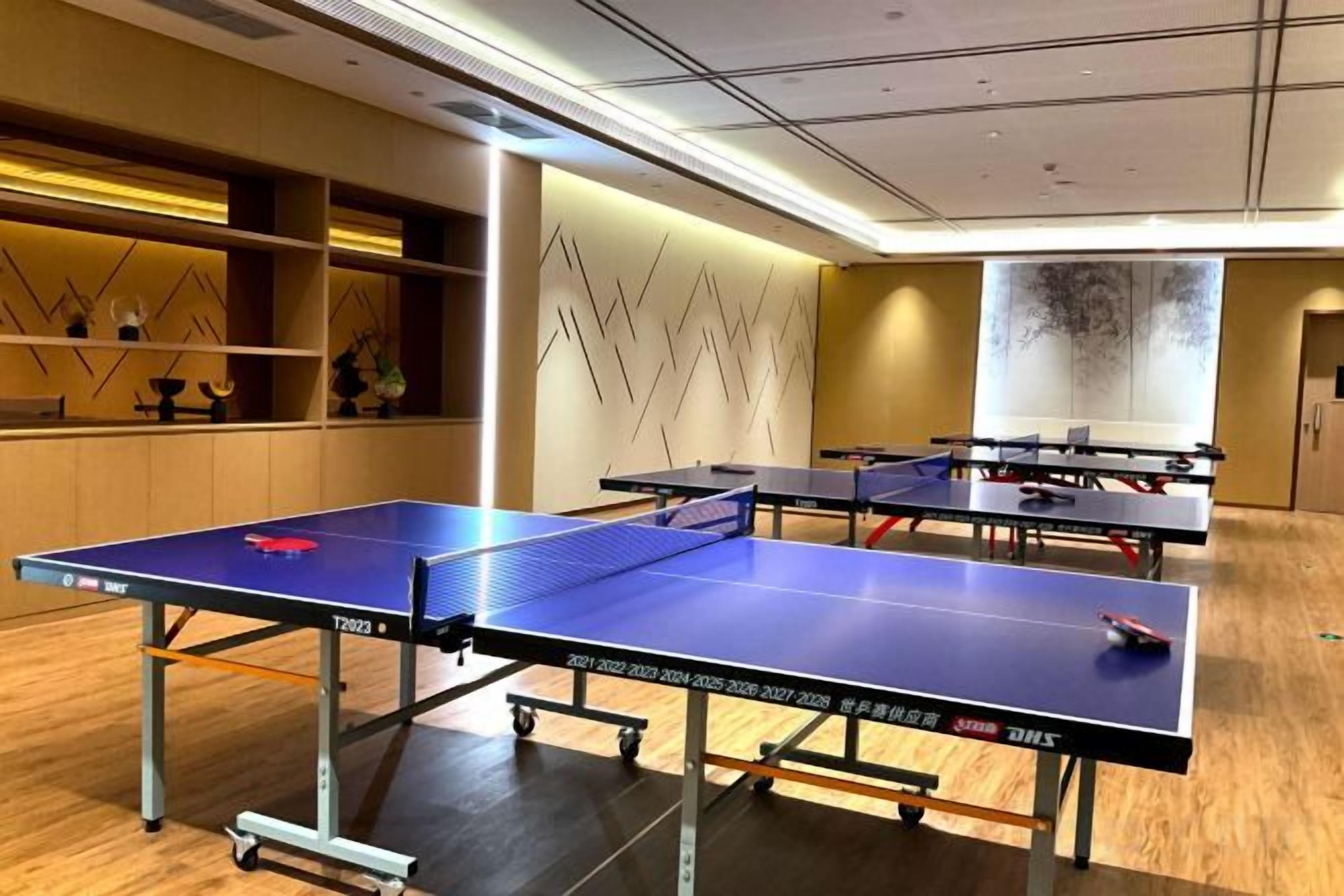 A room with ping pong tables, a wooden floor, and a wall with a geometric pattern.