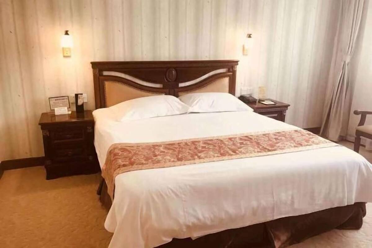 A neatly made bed with a wooden headboard, a bedside table with a lamp, and a wall-mounted light fixture.