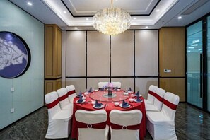 A conference room with a round table, white chairs with red sashes, a chandelier, and a cityscape painting on the wall. - Jingyuan Shuizhuang Hotel (Shanghai)