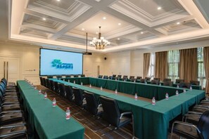 Un salón de conferencias con una larga mesa, sillas, una pantalla de proyector y una araña.
