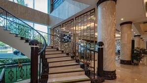 A grand staircase with marble steps and black balusters, leading to a second-floor area with large windows and a view of greenery outside. - Jingyuan Shuizhuang Hotel (Shanghai)
