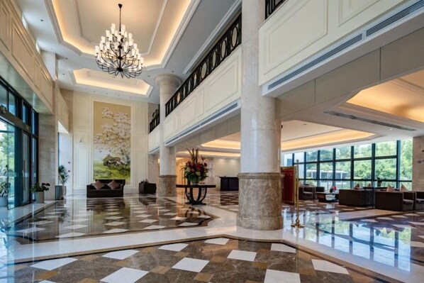 A spacious lobby with a high ceiling, large windows, and a central chandelier.