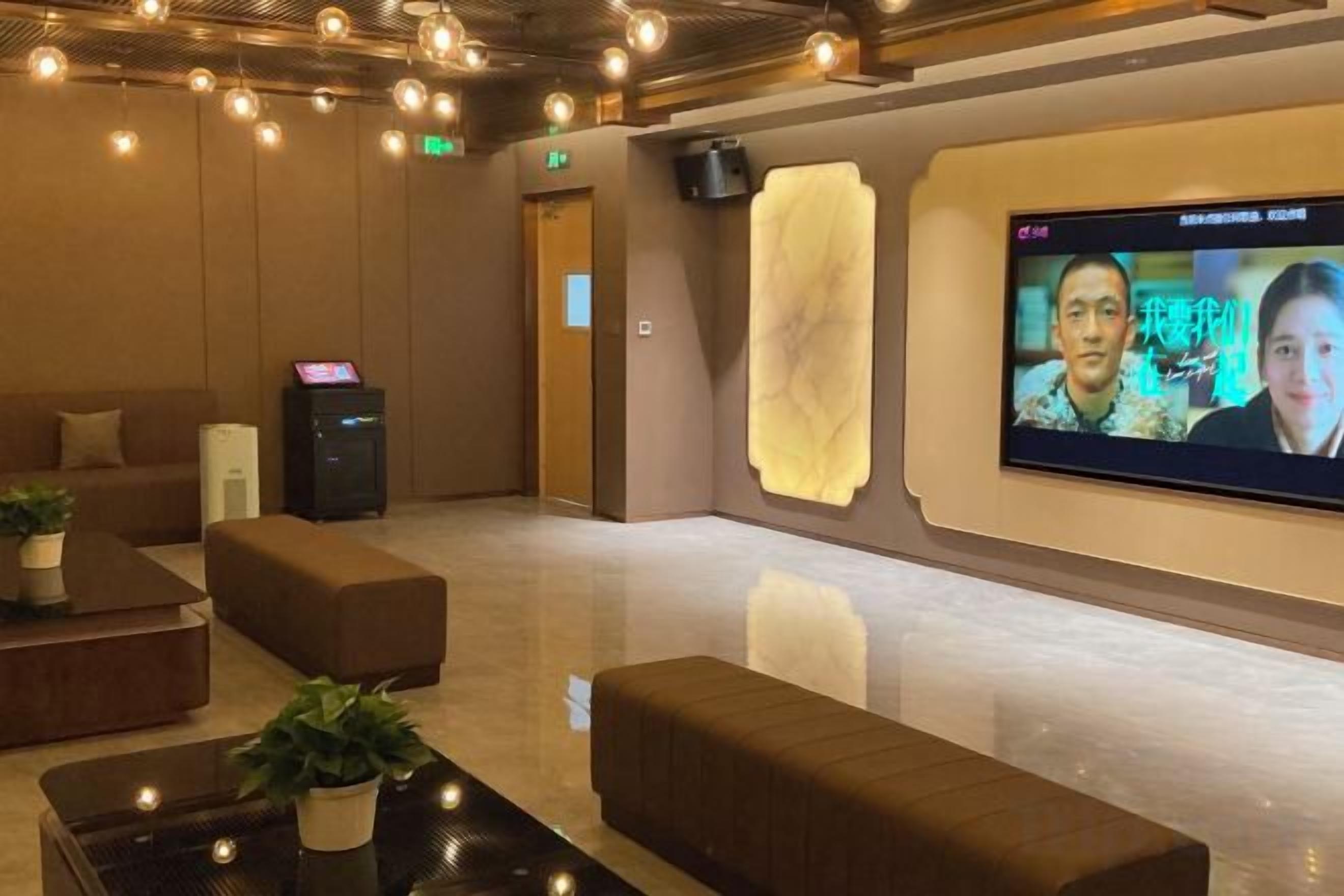 Um hall com assentos, balcão de recepção, tela digital e alto-falante fixado na parede.