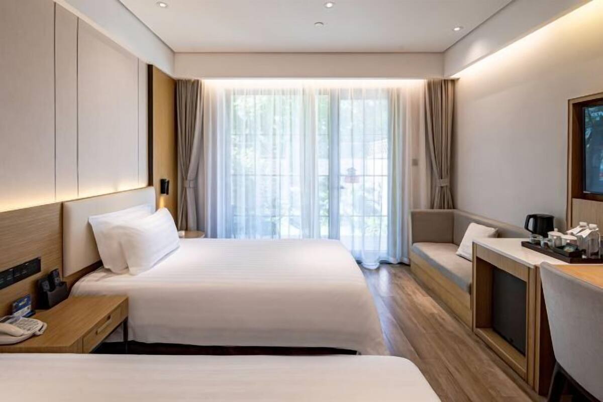 A hotel room with two beds, a desk, a chair, and a large window with curtains.