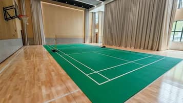 A tennis court with a wooden floor and a green playing surface, surrounded by curtains and a basketball hoop.