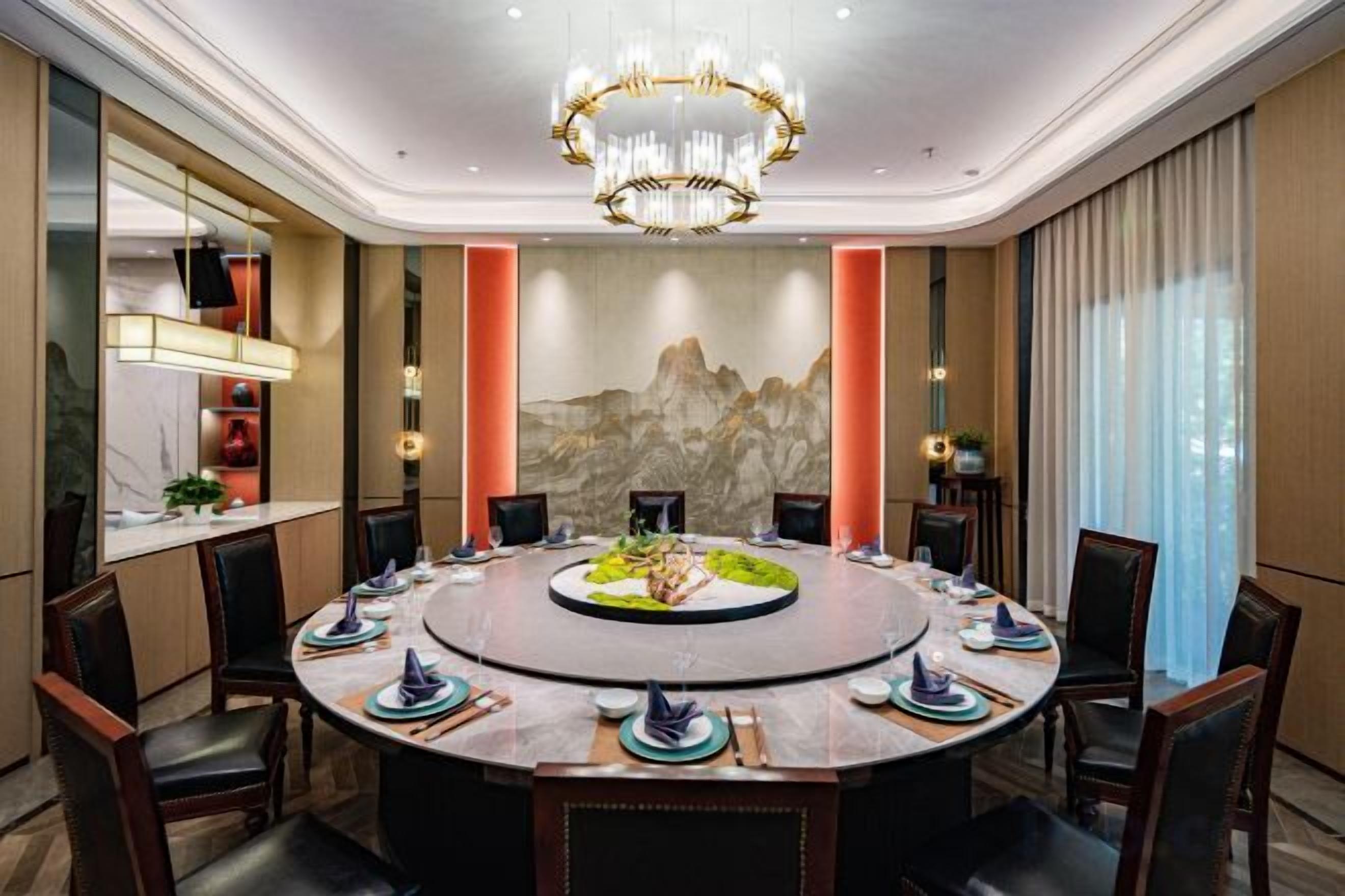 Mesa de jantar redonda com cadeiras, um candelabro e uma pintura de paisagem montanhosa na parede.