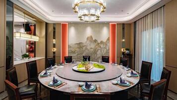 Mesa de jantar redonda com cadeiras, um candelabro e uma pintura de paisagem montanhosa na parede.