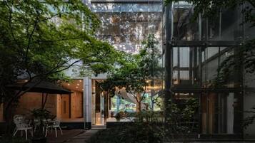 Um edifício moderno com fachada de vidro, área de estar no pátio e vista do interior.