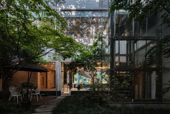 Un bâtiment moderne doté d’une façade en verre, d’un patio avec des espaces de détente en plein air et d’une vue sur l’intérieur.