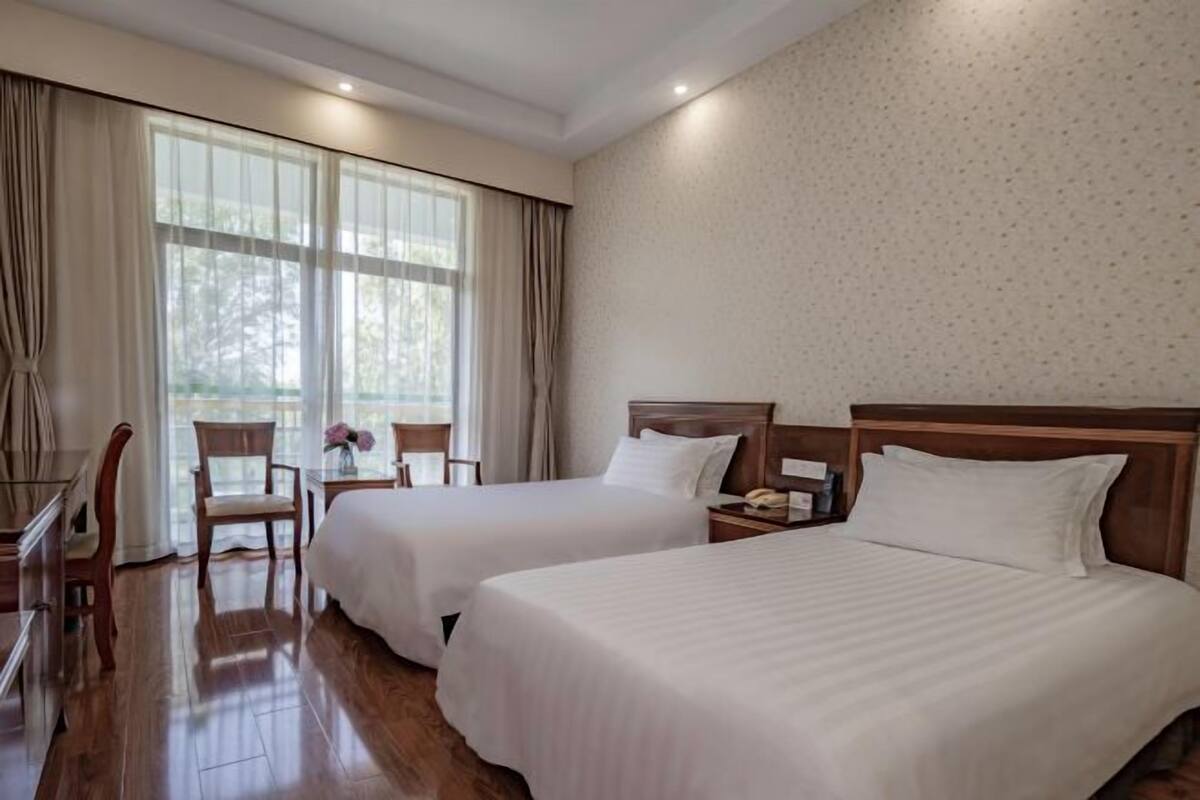 A hotel room with two beds, a desk, a chair, and a window with curtains.