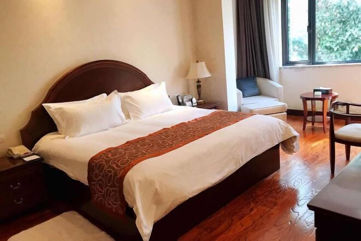 A hotel room with a large bed, a sofa, a chair, a small table, and a window with curtains.