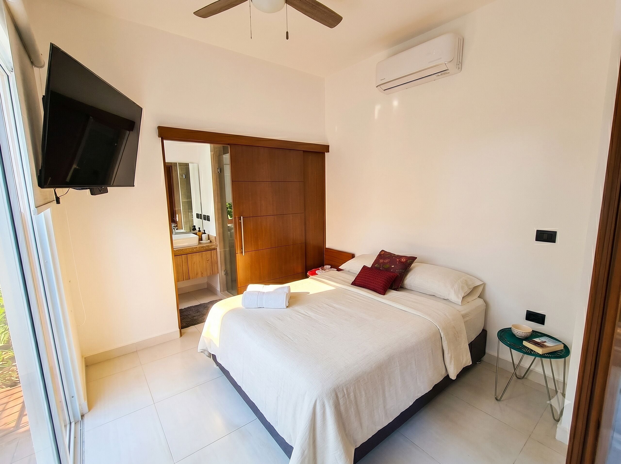 Un dormitorio con cama, televisión, aire acondicionado y una mesita con un cuenco y un libro.