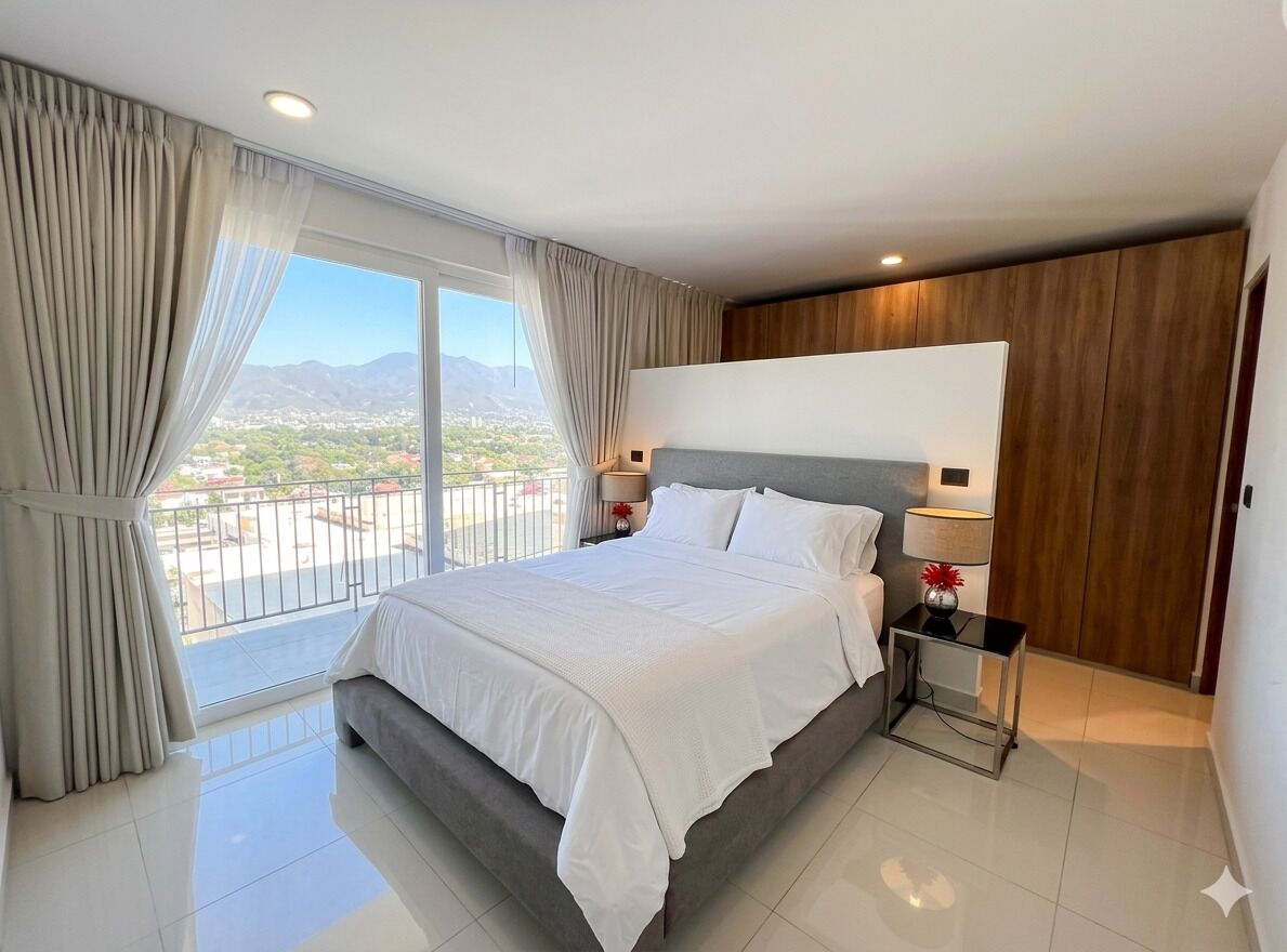A modern hotel room with a large bed, a balcony, and a view of the cityscape.