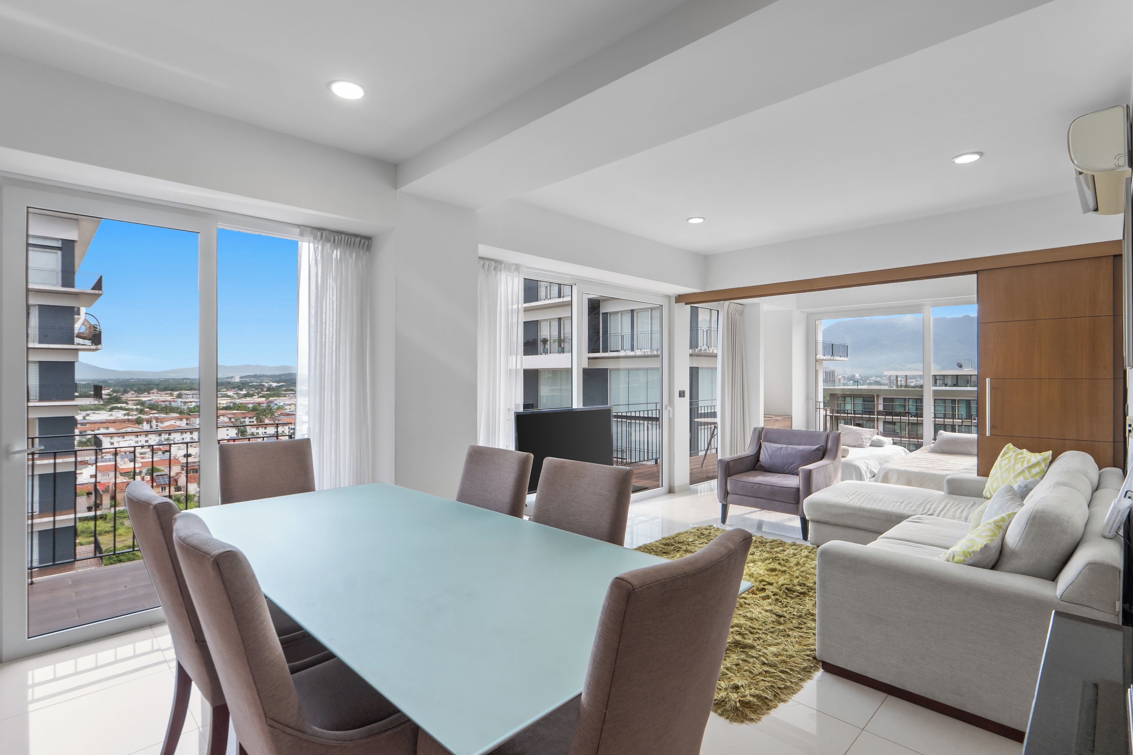 A modern apartment with a dining area, a sofa set, and a balcony with a city view.